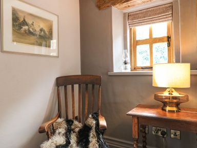 A wooden chair with a fur throw beside a wooden table with a lamp near a window at Balog Farm in Amlwch