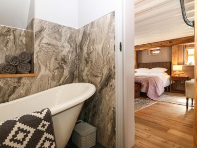 A bathroom with a white bathtub and towels next to a bedroom with a bed and wooden beams at Balog Farm in Amlwch