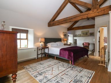 A bedroom with wooden beams a bed with white linens and purple cover and a patterned rug on the floor at Balog Farm in Amlwch