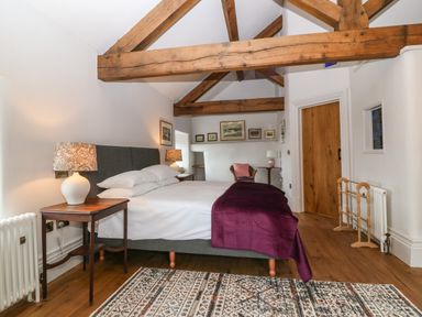 A bedroom with a double bed side tables lamps a chair wooden beams and a wooden door at Balog Farm in Amlwch
