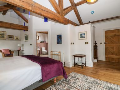 A bedroom with wooden beams a bed with a purple blanket wooden furniture and a door at Balog Farm in Amlwch