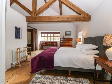 A bedroom with a large bed purple blanket wooden beams wooden furniture and a patterned rug at Balog Farm in Amlwch