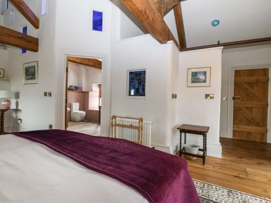 A bedroom with wooden beams a wooden door a small table and an open doorway to a bathroom at Balog Farm in Amlwch