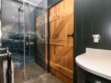 A bathroom with a glass shower enclosure featuring a wave pattern on the wall a wooden barn door and a white countertop at Balog Farm in Amlwch