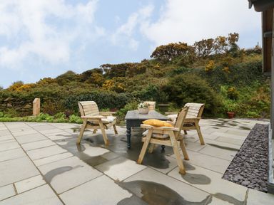 An outdoor patio with wooden chairs and a table surrounded by greenery at Balog Farm in Amlwch