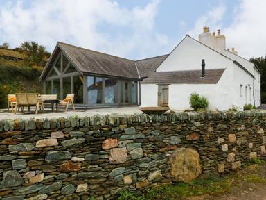 A white house with a stone wall and wooden patio furniture at Balog Farm in Amlwch