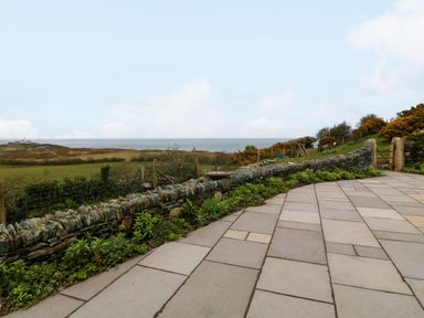 A stone wall beside a tiled patio with grassy fields and the sea in the background at Balog Farm in Amlwch
