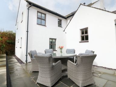 An outdoor patio area with a round glass table and six wicker chairs with cushions at Balog Farm in Amlwch