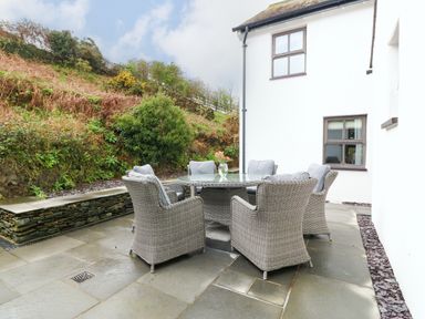 An outdoor patio with a glass table and six wicker chairs next to a white building at Balog Farm in Amlwch