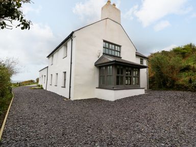 The exterior of a two story white house with multiple windows and a gravel driveway at Balog Farm in Amlwch