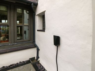 An outdoor corner of a building with a window black drainpipe and an electric vehicle charging point mounted on a white wall at Balog Farm in Amlwch