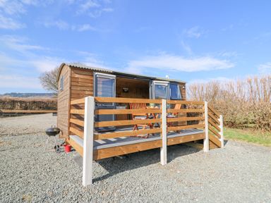 A small wooden cabin with a raised deck and outdoor furniture on a gravel area at Elan in Rhayader