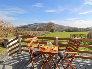 A wooden patio table with two chairs and breakfast setting overlooking a green field and hills at Elan in Rhayader