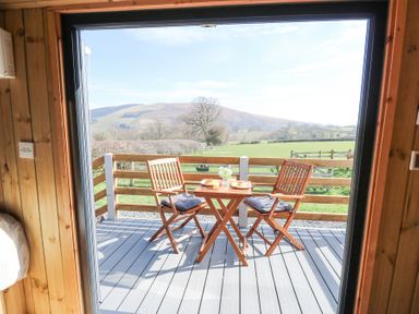 A wooden deck with two chairs and a table with breakfast overlooking green fields and hills at Elan in Rhayader