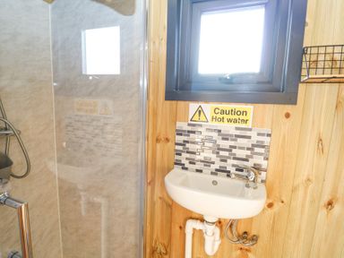 A bathroom with a small sink under a window and a caution hot water sign at Elan in Rhayader