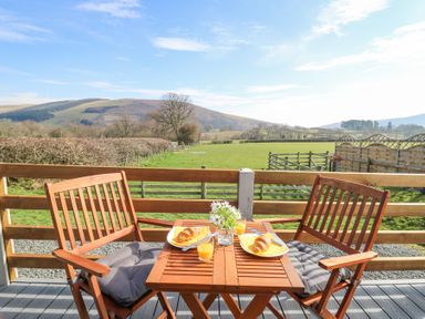 A wooden outdoor table with two chairs overlooking a green field and hills at Elan in Rhayader