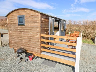A small wooden cabin with an outdoor grilling area and patio furniture on a gravel surface at Elan in Rhayader