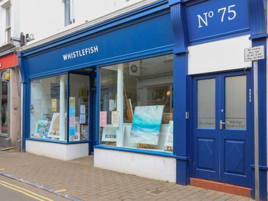 A storefront with blue signage and windows displaying paintings and cards at The Penthouse in Salcombe