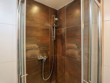 A shower area with a handheld showerhead and brown tiled walls at The Penthouse in Salcombe