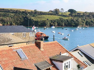 Boats on water near stone and tiled roof buildings with grassy hillside in the background at The Penthouse in Salcombe
