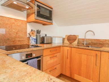 A kitchen with a stove oven microwave toaster and sink with wooden cabinets at The Penthouse in Salcombe