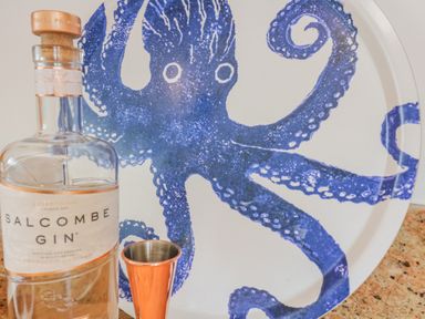 A bottle of Salcombe gin and a copper jigger in front of a plate with a blue octopus design