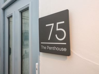 A gray door next to a black sign with white text showing number 75 and The Penthouse