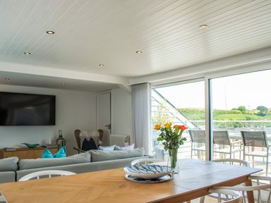 A dining table with a vase of flowers and plates next to a sofa and a large window with a balcony view at The Penthouse in Salcombe