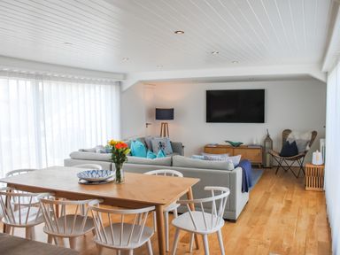 A dining table with chairs and flowers in a living room with a couch and a wall-mounted TV at The Penthouse in Salcombe