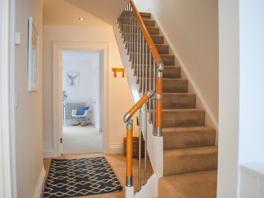 A hallway with a carpeted staircase and a patterned rug leading to a room with a chair and radiator at The Penthouse in Salcombe