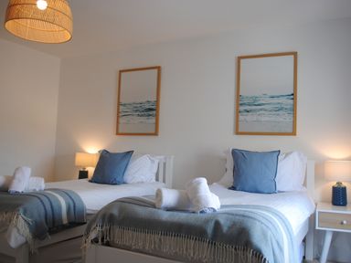 A bedroom with two single beds each with blue pillows and blankets with rolled white towels on them at The Penthouse in Salcombe
