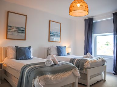 A bedroom with two single beds blue pillows striped blankets and framed ocean pictures at The Penthouse in Salcombe