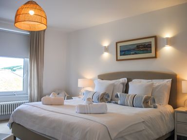 A bedroom with a large bed towels on the bed bedside tables lamps and a window at The Penthouse in Salcombe