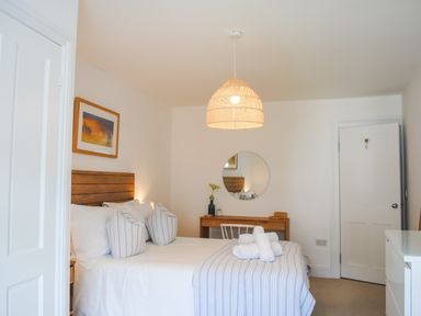 A bedroom with a bed with striped pillows and blanket a desk with a round mirror and a door at The Penthouse in Salcombe