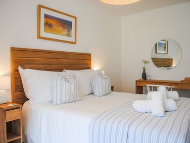 A bedroom with a wooden bedframe and white linens a wooden desk with a round mirror and a lamp on a nightstand at The Penthouse in Salcombe