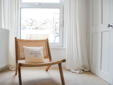 A wooden chair with a cushion near a window with white curtains at The Penthouse in Salcombe