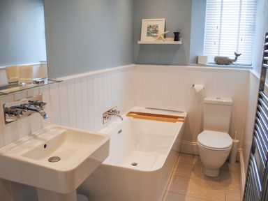 A bathroom with a sink bathtub and toilet with window and shelf at The Penthouse in Salcombe