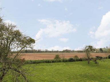 A grassy lawn with trees and shrubs overlooking a plowed field and distant treeline at Lugg View in Cross Keys near Hereford
