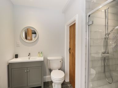 A bathroom with a sink cabinet a round mirror a toilet a wooden door and a glass shower enclosure at Lugg View in Cross Keys near Hereford