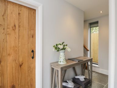 A hallway with a wooden door a wooden table with a floral vase and folded towels near a window at Lugg View in Cross Keys near Hereford