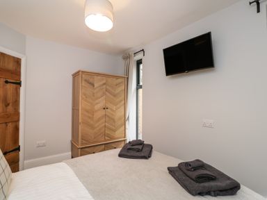 A bedroom with a bed with folded towels a wooden wardrobe a wall mounted television and a wooden door at Lugg View in Cross Keys near Hereford