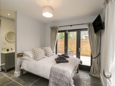 A bedroom with a bed towels and pillows next to glass doors with curtains and a wall-mounted television at Lugg View Cross Keys near Hereford