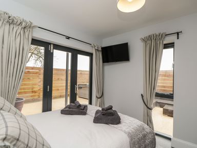 A bedroom with a bed and rolled towels on it a wall-mounted television and windows with curtains at Lugg View in Cross Keys near Hereford