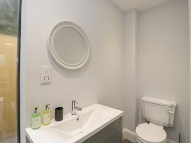 A bathroom with a sink a round mirror and a toilet at Lugg View in Cross Keys near Hereford