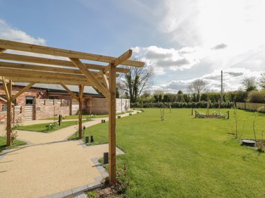 A garden area with a wooden pergola, pathways, green lawn, small trees, and a brick building at Lugg View in Cross Keys near Hereford