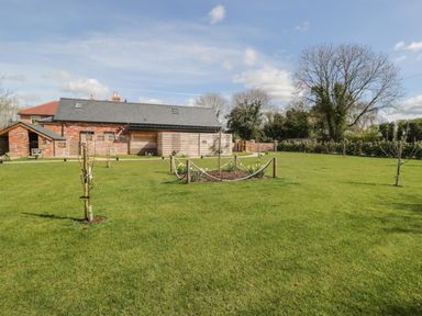 A grassy garden area with young trees and a building with brick and wood siding at Lugg View in Cross Keys near Hereford