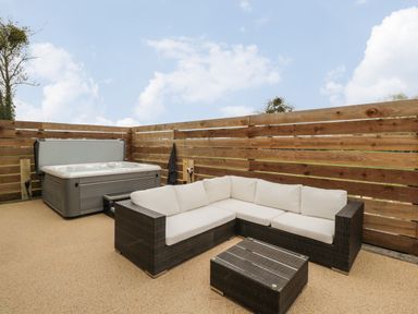 An outdoor patio with a hot tub and wicker sofa with white cushions and a matching wicker coffee table at Lugg View in Cross Keys near Hereford