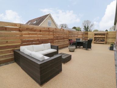 An outdoor patio with a sectional sofa and cushions a small table a dining table with chairs potted plants and stacked firewood at Lugg View Cross Keys near Hereford