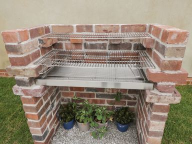A brick outdoor barbecue grill with metal racks and potted plants underneath at Lugg View in Cross Keys near Hereford