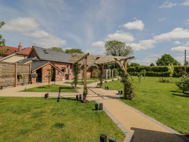 A garden with a wooden pergola and pathways near a brick building at Lugg View in Cross Keys near Hereford